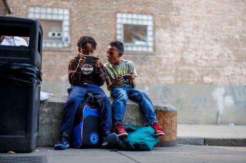 From left, Eduardo Rodriguez, 10, and his brother Andres Gonzalez , 9, both from Venezuela, play with cell phones after coming home from school while sitting outside their shelter on North Ogden Avenue Monday Sept. 9, 2024, in Chicago. Recently the city announced it would close the migrant shelter on North Ogden Avenue.